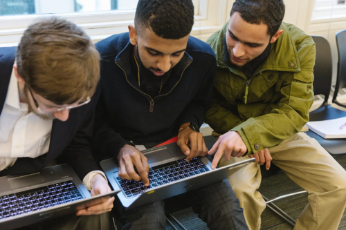 Three people look at laptops together.